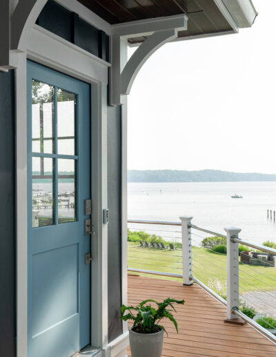 Covered porch entry with exposed rafters, blue front door, and view of the water beyond.