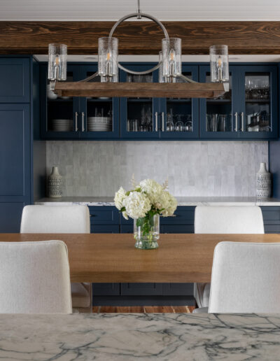 Dining space with blue built-ins, exposed beams, and white chairs.